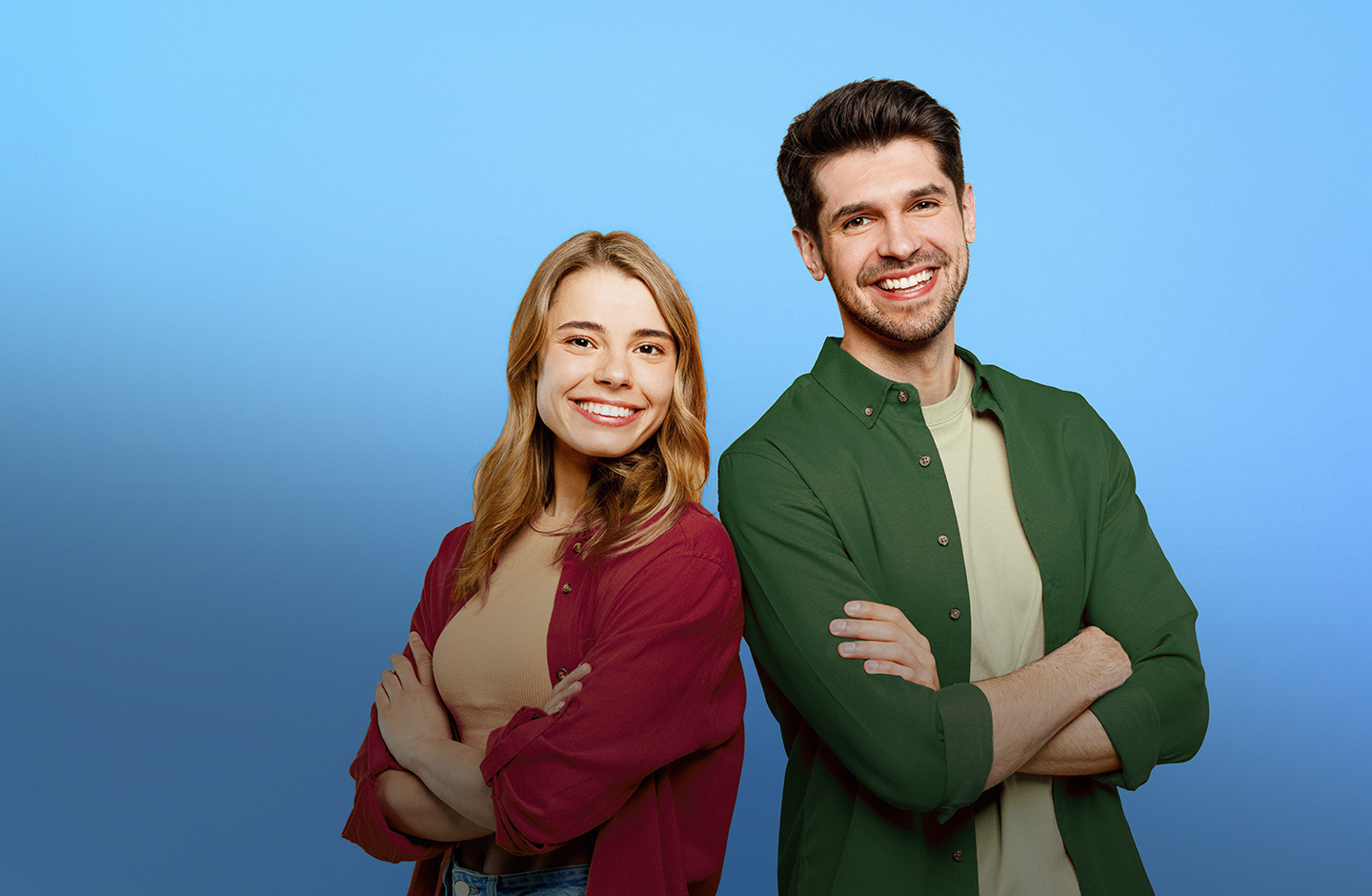Eine junge Frau und ein junger Mann strahlen. Sie stehen Rücken an Rücken und haben die Arme vor der Brust verschränkt. 