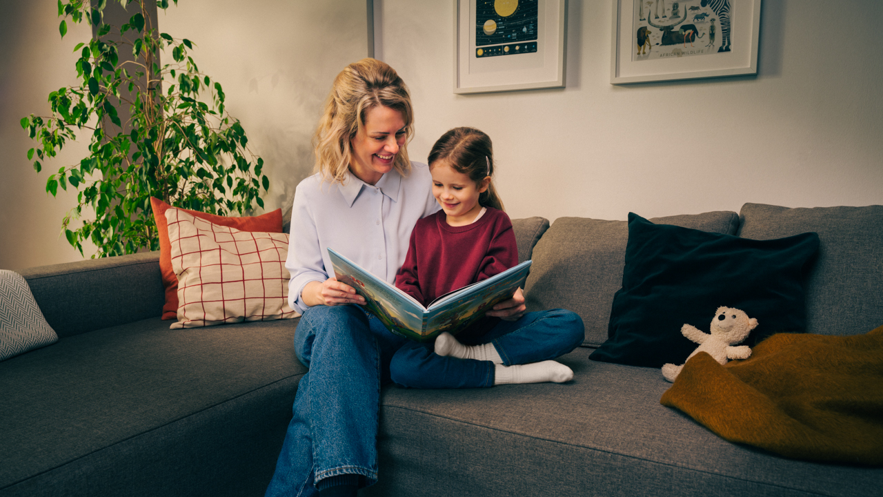 eine Mutter sitzt auf dem Sofa und liest gemeinsam mit ihrer Tochter ein Buch