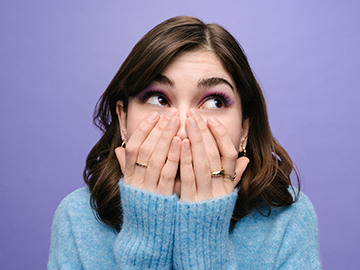 eine Jugendliche mit blauem Pullover und langen braunen Haaren hält sich den Mund zu