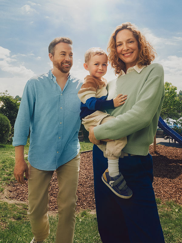Eine Familie steht auf einem Spielplatz. Die Mutter hat das Kind im Arm.